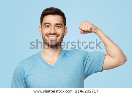 Young strong sporty athletic man in casual t-shirt, showing biceps after training in gym, isolated on blue background Royalty-Free Stock Photo #2146202717
