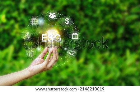 Hand holding light bulb with ESG icon concept for environmental, social, and governance in sustainable and ethical business on the Network connectionon a green nature background.                   