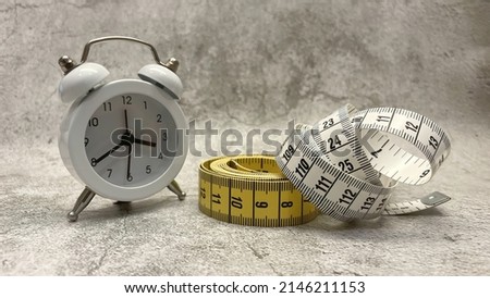 Tape measure and clock on gray floor and background