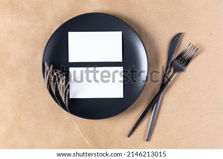 Blank white paper card on plate for mock up with dried spikelets decoration on craft beige background. Flatlay, top view with copy space, mockup. Minimal boho style