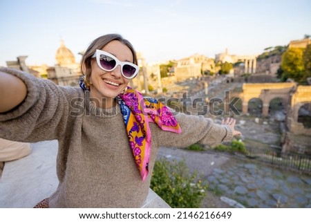 Portrait of a cheerful woman in front of the Roman Forum, ruins at the center of Rome on a sunset. Concept of traveling famous landmarks in Italy. Caucasian woman wearing colorful shawl and sunglasses