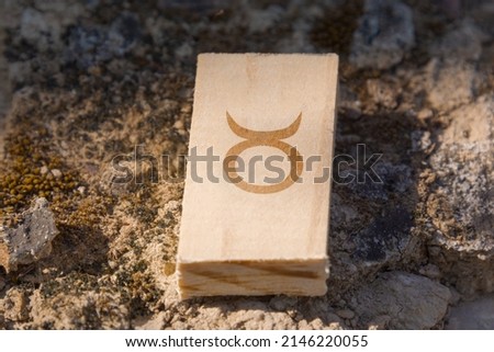 Close-up shot of a piece of wood with a zodiac sign engraved on it, especially the Taurus sign