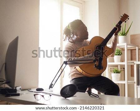 Young man is singing and playing guitar while making an audio recording at home