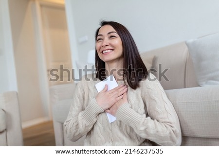 Cheerful Asian woman presses received letter to the chest, at homer, receiving invitation or good news about approved loan, mortgage, tax, insurance, getting notice about acceptance of statement Royalty-Free Stock Photo #2146237535