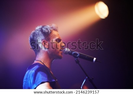 Shot of a solitary musician playing guitar and singing into a microphone. This concert was created for the sole purpose of this photo shoot, featuring 300 models and 3 live bands. All people in this Royalty-Free Stock Photo #2146239157
