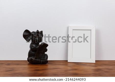 
Minimalist still life of a customizable picture frame and elephant figure. Wood and white background