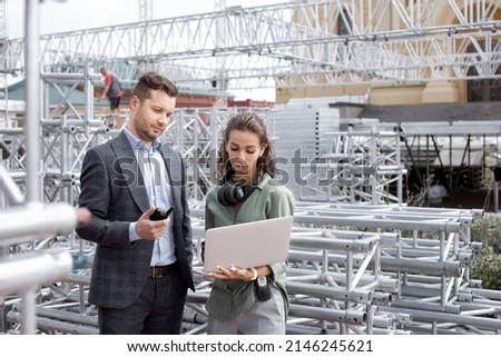 
Event managers discuss stage construction. Installation of stage equipment and preparing for a live concert open air. Event manager portrait. Summer music city festival. Teamwork. Royalty-Free Stock Photo #2146245621
