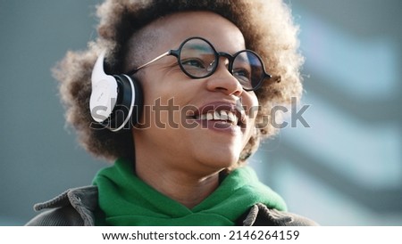 African american happy woman wearing eyeglasses and headphones while walking outdoors Royalty-Free Stock Photo #2146264159