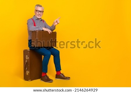 Full body photo of mature attractive male advertise you traveling tour sitting retro luggage isolated on yellow color background
