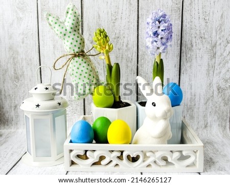 Decorative Easter composition, on a white wooden background is a wooden box with spring flowers, colorful Easter eggs and a white rabbit.  Front view, Easter holiday concept.  Close-up.