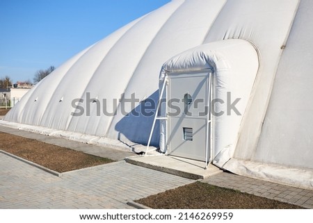 Inflatable air dome stadium. Inflated Tennis air dome or Tennis bubble arena entrance door into structure equipped with airlock either two sets of parallel doors or a revolving door or both. Royalty-Free Stock Photo #2146269959