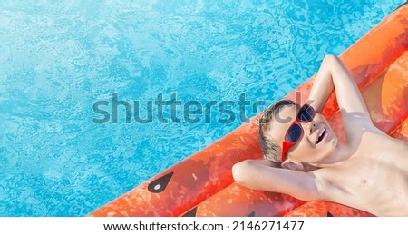 Happy nine years old Caucasian child (boy) in red sunglasses having fun on inflatable ring (air mattress) in swimming pool. Kid water toys, summer holiday, resort. Family beach vacation. Copy space.