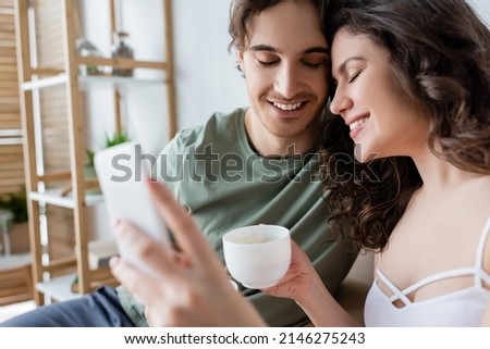 cheerful young couple with closed eyes holding cups and taking selfie