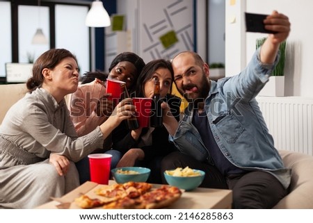 Diverse group of colleagues using mobile phone to take pictures at office party with drinks after hours. People doing fun leisure activity with smartphone, having beer bottles and pizza.