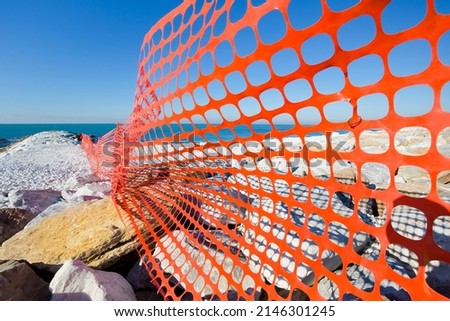 Perforated safety orange plastic grid to delimit a construction site areas by the sea 