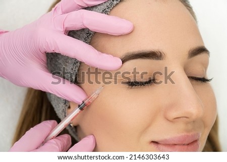 Close-up of the hands of an expert cosmetologist injecting botox into a woman's forehead. Correction of forehead and eye wrinkles with botulinum toxin. Royalty-Free Stock Photo #2146303643