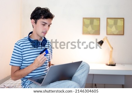 Man sitting on bed at home and using mobile app for online shopping and using credit card to pay. 