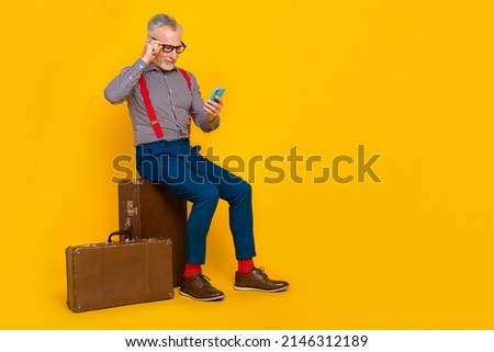 Full length photo of mature blogging man sit bag surfing in social network modern technology isolated on yellow color background