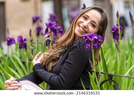 Happy young woman sitting near flowers while looking at camera