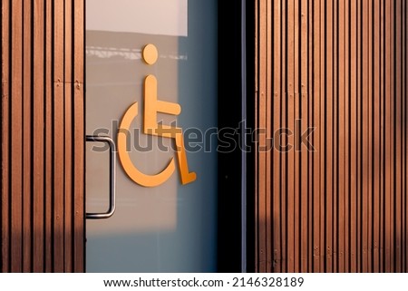 Accessible wheelchair Restroom Sign on glass sliding Door with wooden wall in Public area
