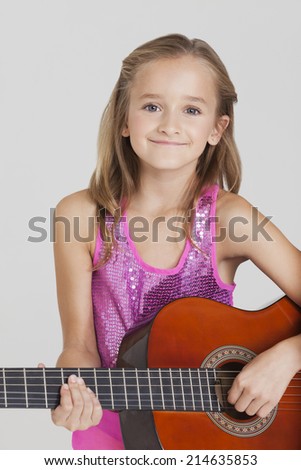 Portrait of young girl playing guitar against gray background