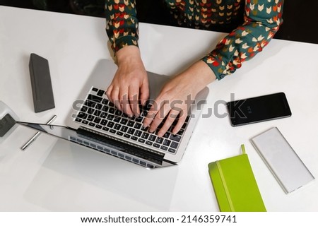 Female hand typing keyboard on laptop. Unrecognizable elegant woman working on computer at office. Start or finish of a work day. Workplace. Green notebook, phone, clock. Top view. Time for work.