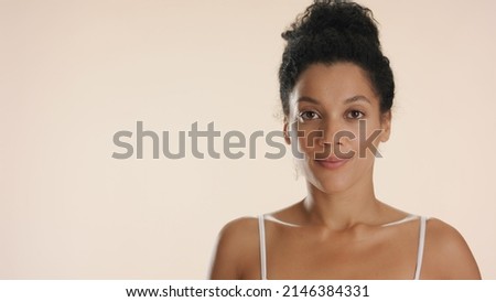 Close-up beauty portrait of young African American woman who looks at camera standing against white background | Skin moisturizing concept