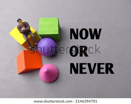 Top view miniature people and colored block with text NOW OR NEVER on gray background.