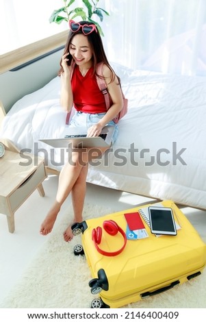 Young happy and excite Asian female traveler getting ready for a summer holiday trip vacation searching for travel information using laptop in bedroom.