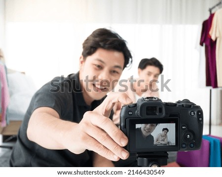 Asian young blogger man push the button on camera and record video live after prepared fashion clothes for review in bedroom at home