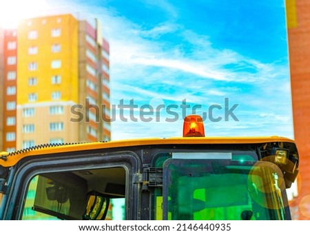 Warning orange beacon flashing in soft focus on roof car or tractor of emergency, utilities, lifeguards, support and service vehicle against the background of a high-rise in the city. 