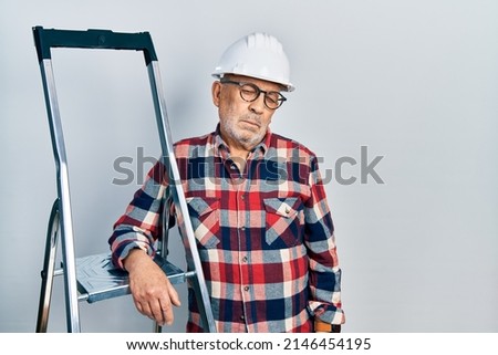 Handsome mature handyman close to construction stairs wearing hardhat looking sleepy and tired, exhausted for fatigue and hangover, lazy eyes in the morning. 