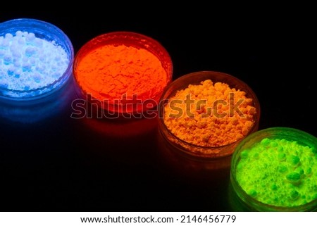 Fluorescent organic materials powder of red, yellow, green color for production OLED inside of glasses bottles in UV light. Royalty-Free Stock Photo #2146456779
