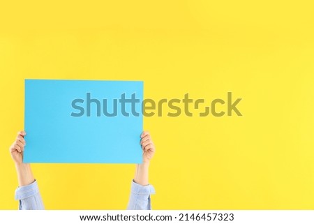Female hands holding blank banner on yellow background