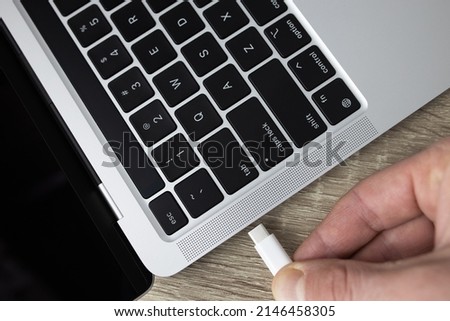 Connect the usb type-c cable to the computer. Connecting the usb type-c cable to the charging connector close-up. A man connects usb type-c cable to a laptop connector. High quality photo Royalty-Free Stock Photo #2146458305