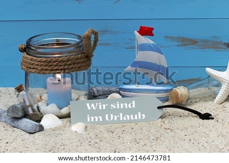 Lantern with shells and starfish in the sand with the text wir sin in Urlaub.Wir sin in Urlaub means translated we are on vacation.