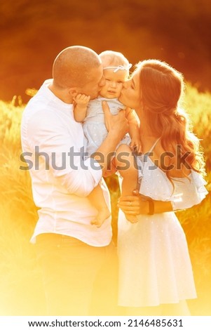 Young parents hold cute baby girl in caring arms at the park, lovely mom and dad kiss beautiful daughter, smile, enjoy tender family moments, parenthood and childhood concept. High quality photo