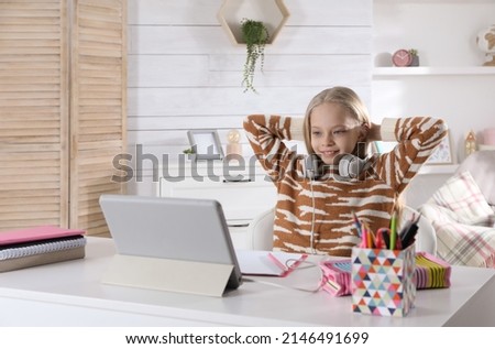 Cute little girl with modern tablet studying online at home, space for text. E-learning