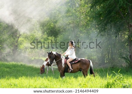Young woman in white dress with horse. Woman riding red horse in the garden. Beautiful bride in a dress riding a horse. Royalty-Free Stock Photo #2146494409