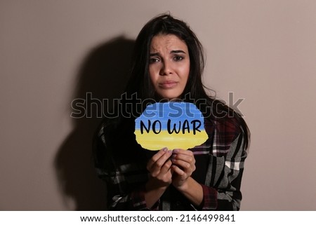 Sad woman holding paper with phrase No War near beige wall