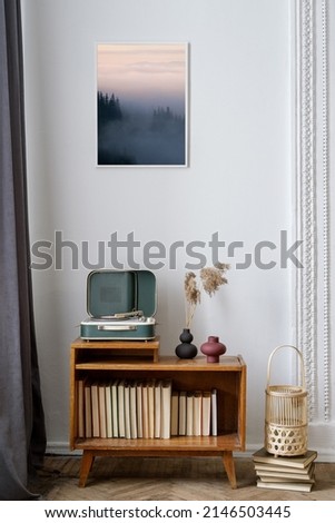 Vertical view of cozy living room with vinyl player on wooden sideboard with books, under art picture. Retro style decor, vintage furniture and analog or nostalgic sound equipment in apartment