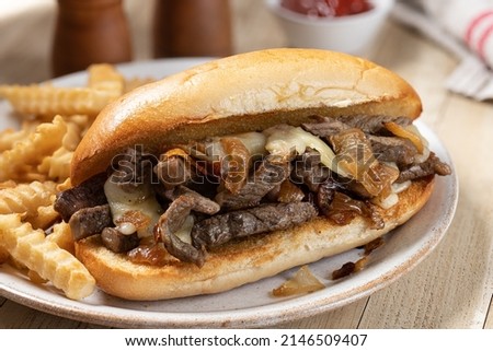 Closeup of philly cheesesteak sandwich made with steak, cheese and onions on a toasted hoagie roll with french fries on a plate Royalty-Free Stock Photo #2146509407