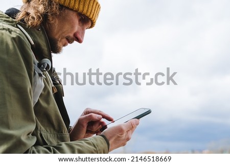 The guy looks at the phone and types a message with his finger, a tourist on a hike orients himself with the help of a gadget, a man with a smartphone in his hands, calls for help in the forest