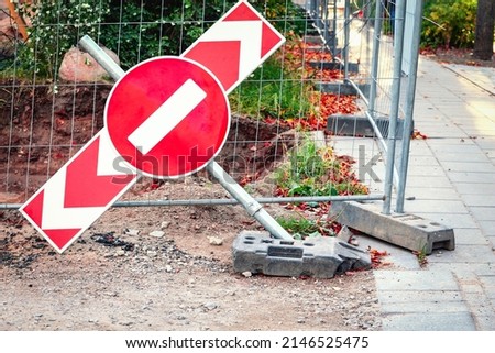 Red stop road sign on red arrow sign falling on ground near construction site and concrete road