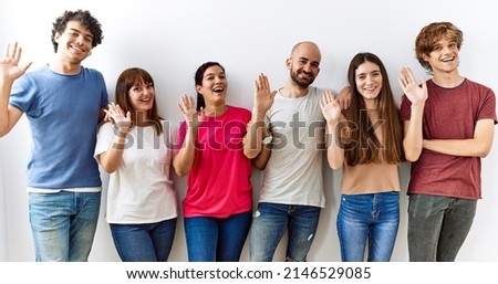 Group of young friends standing together over isolated background waiving saying hello happy and smiling, friendly welcome gesture  Royalty-Free Stock Photo #2146529085
