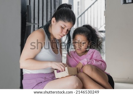 mother and daughter looking at the box sent to her by her husband who lives abroad. sad girl because her father is far away and cannot come to visit her. concept of abandonment.