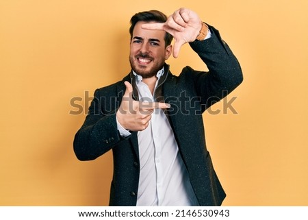 Handsome caucasian man with beard wearing elegant business jacket smiling making frame with hands and fingers with happy face. creativity and photography concept. 