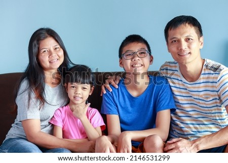 Portrait of Thai family with parents, sons and daughters. Family of four is a picture that feels full of love and warmth.sitting on the sofa in the house Father and mother take good care of children