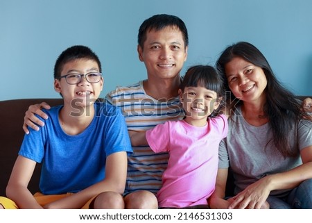Portrait of Thai family with parents, sons and daughters. Family of four is a picture that feels full of love and warmth.sitting on the sofa in the house Father and mother take good care of children