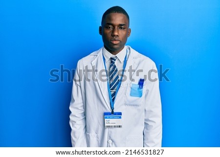 Young african american man wearing scientist uniform with serious expression on face. simple and natural looking at the camera. 